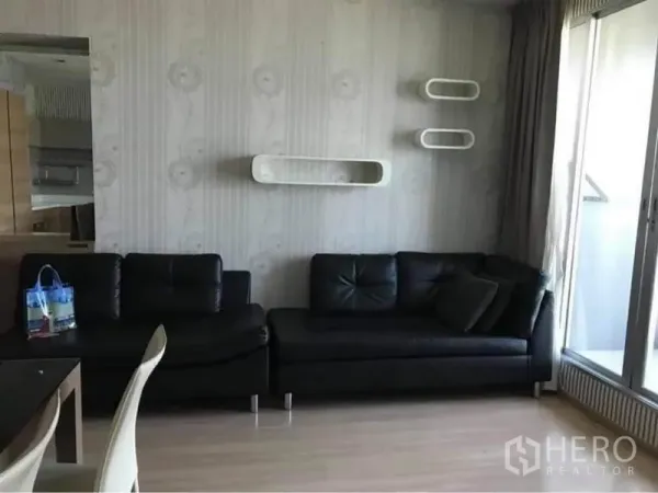 คอนโด ให้เช่าหรือขายในPhaya Thai, Bangkok - ห้องนั่งเล่นสว่าง โซฟาหนังสีดำ ชั้นติดผนัง และประตูกระจกสไลด์ออกสู่ระเบียง