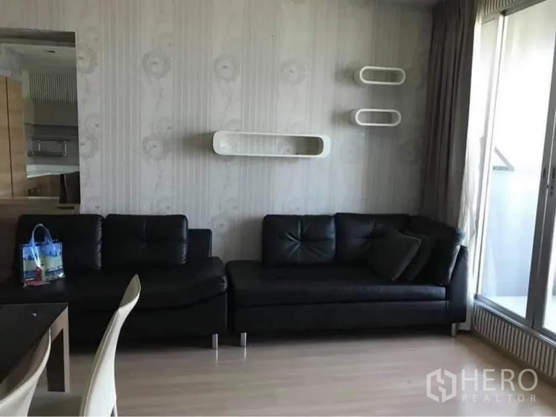 คอนโด ให้เช่าหรือขายในPhaya Thai, Bangkok - ห้องนั่งเล่นสว่าง โซฟาหนังสีดำ ชั้นติดผนัง และประตูกระจกสไลด์ออกสู่ระเบียง