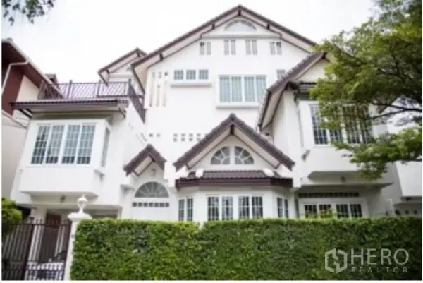 Detached House for rent in Khlong Toei, Bangkok - Front exterior of a large white detached house with gabled roof, bay windows and a tall green hedge.