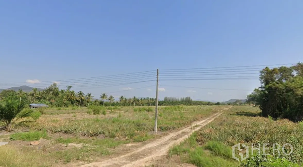 Land for sale in Mueang Prachuap Khiri Khan, Prachuap Khiri Khan - Open field plot with dirt track, utility poles, and distant hills.