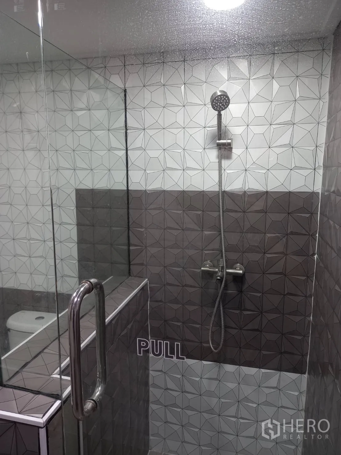 公寓 出租在Khlong Toei, Bangkok - 现代浴室，玻璃淋浴房与几何图案墙砖。