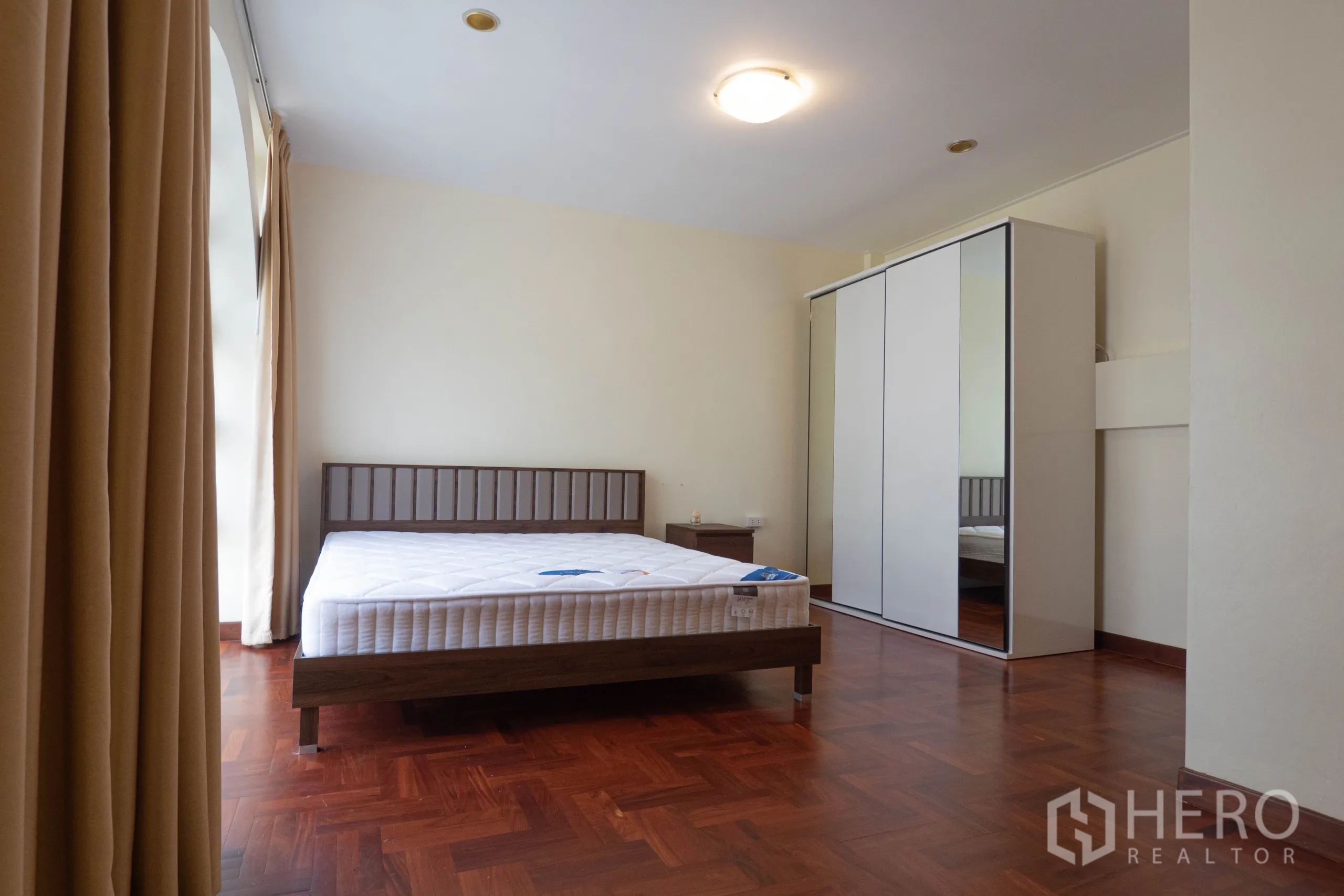 Townhouse for rent in Khlong Toei, Bangkok - Spacious bedroom with bed, bedside table and mirrored wardrobe on parquet flooring.
