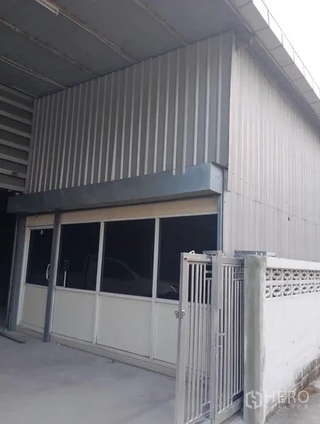Warehouse for rent in Huai Khwang, Bangkok - Front office-style entrance with sliding glass doors beside a metal gate under the warehouse canopy.