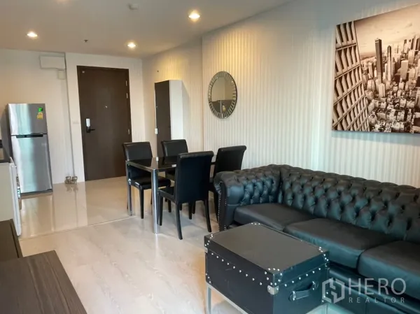 Condominium for sale in Sathon, Bangkok - Open-plan living space with black sofa, four-seat dining table and a compact kitchenette with stainless refrigerator.