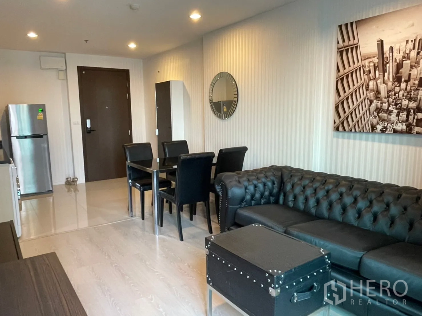 Condominium for sale in Sathon, Bangkok - Open-plan living space with black sofa, four-seat dining table and a compact kitchenette with stainless refrigerator.