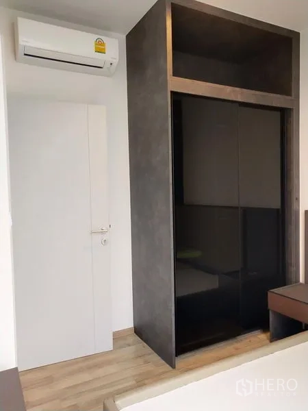 Condominium for rent in Chatuchak, Bangkok - Bedroom corner with glossy sliding-door wardrobe and a wall-mounted air conditioner.