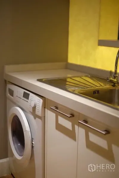 Condominium for rent in Watthana, Bangkok - Laundry corner with front-loading washing machine, sink, and under-counter storage.