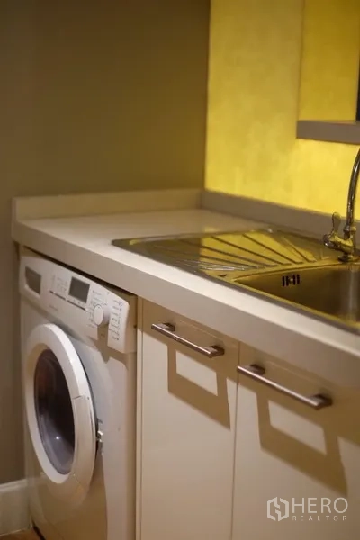 Condominium for rent in Watthana, Bangkok - Laundry corner with front-loading washing machine, sink, and under-counter storage.