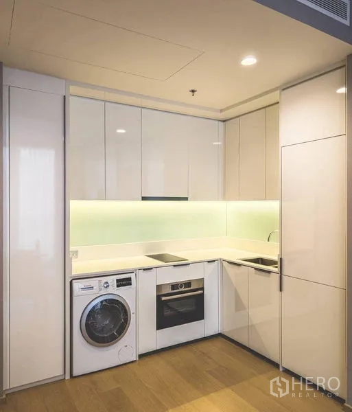Condominium for rent in Bang Rak, Bangkok - Compact L-shaped kitchen with glossy cabinets, built-in oven, cooktop and washer-dryer.