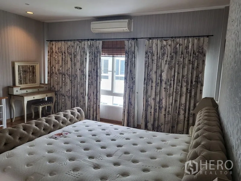Townhouse for rent in Wang Thonglang, Bangkok - Bright bedroom with floral curtains, vanity desk and wall air conditioner.