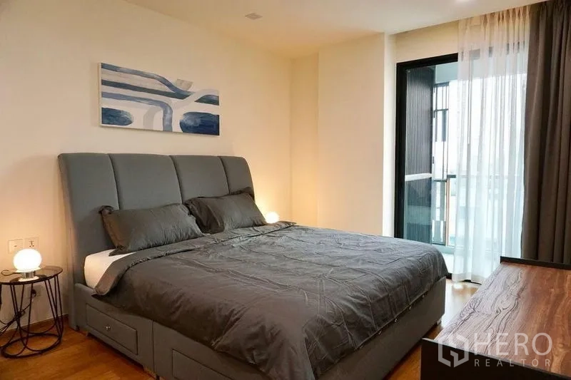 คอนโด ให้เช่าในKhlong Toei, Bangkok - ห้องนอนเตียงใหญ่บุผ้าสีเทา พร้อมโคมไฟและประตูบานเลื่อนออกสู่ระเบียง