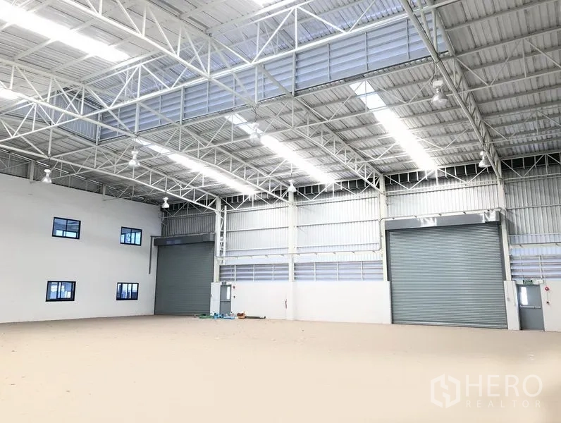 工厂 出租或出售在Bang Sao Thong, Samut Prakan - 开阔仓库大厅，配两樘大型卷帘门、通风百叶与明亮天窗。