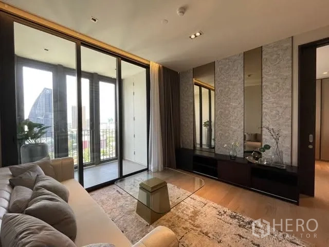 Condominium for rent or sale in Khlong Toei, Bangkok - Contemporary lounge with sliding glass to the balcony, mirrored feature wall, and area rug.