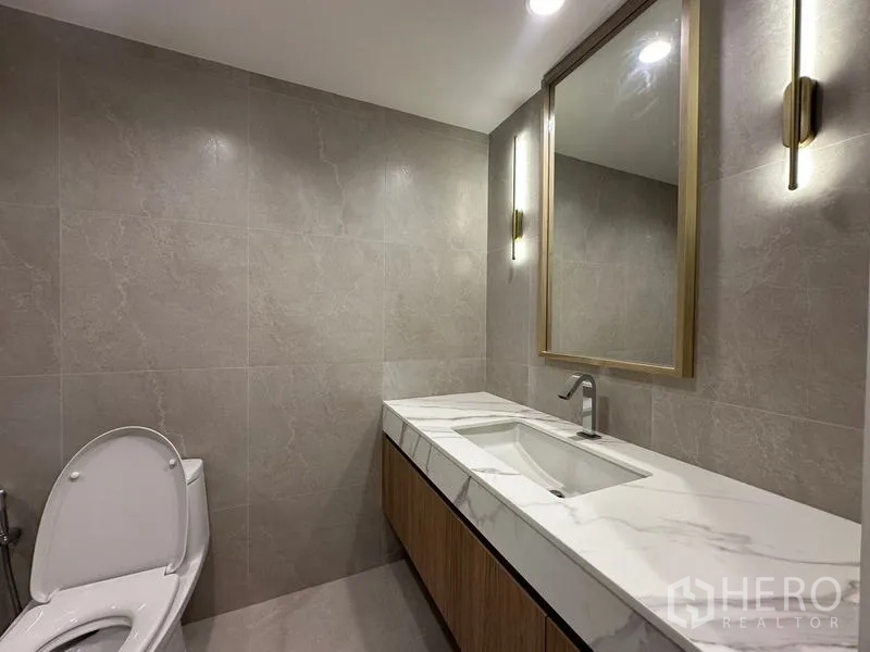 Home Office for rent in Khlong Toei, Bangkok - Elegant powder room with marble-top vanity, framed mirror and wall sconces.