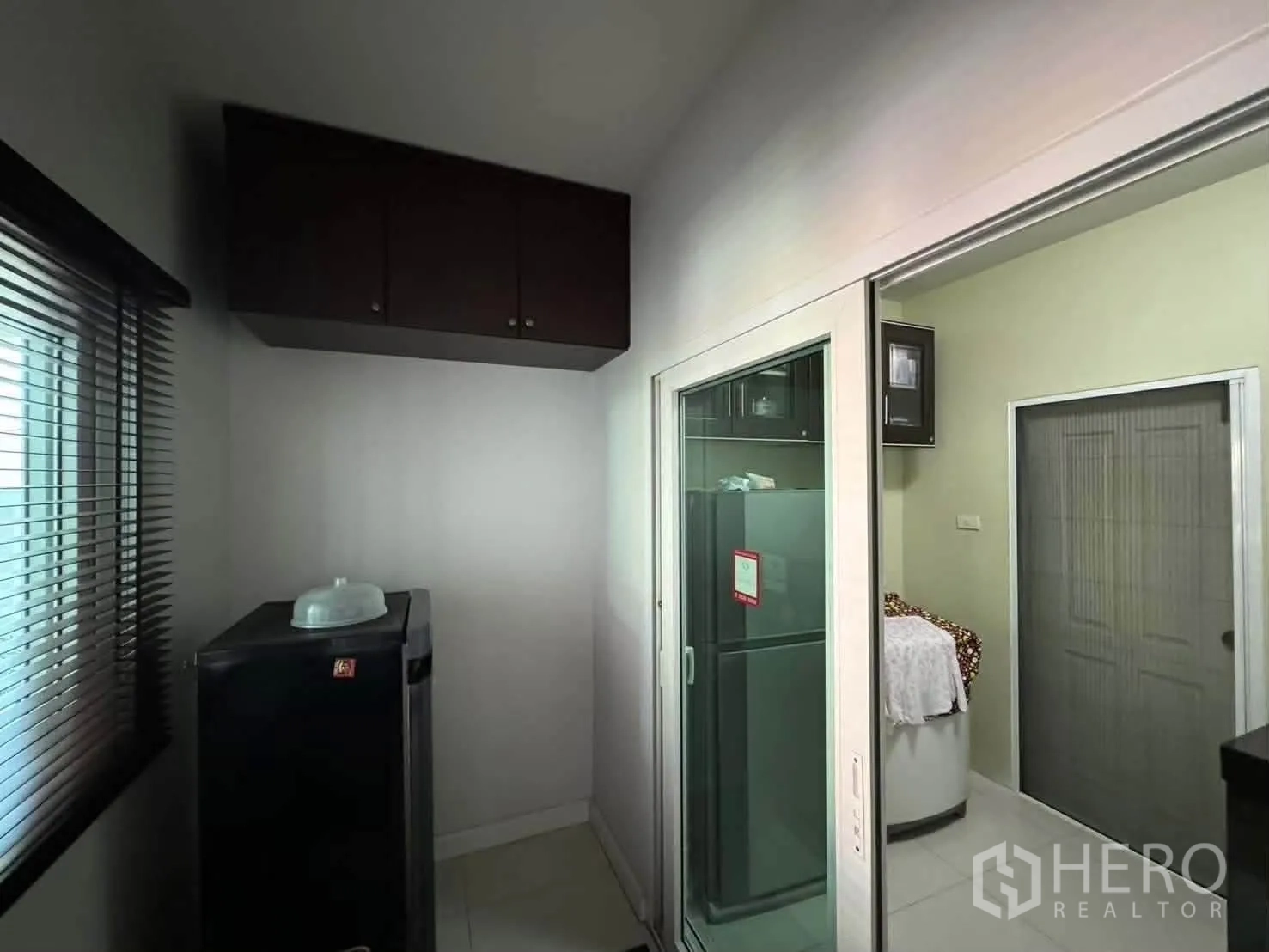 Detached House for rent in Watthana, Bangkok - Utility area with a sliding glass door, refrigerator, window blinds, and overhead cabinets.