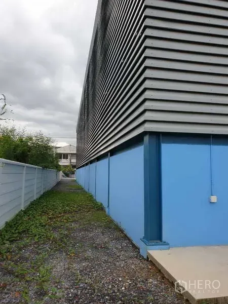 工厂 出售在Sai Noi, Nonthaburi - 工厂侧立面，波纹金属板覆于蓝色墙体，沿围墙而建。