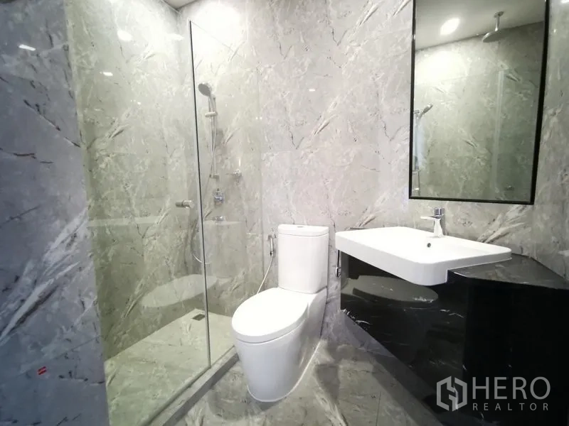 Condominium for rent or sale in Watthana, Bangkok - Second bathroom with glass shower enclosure, white vanity and marble walls.
