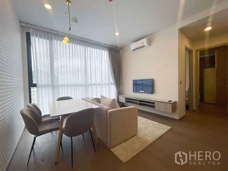 Condominium for rent in Ratchathewi, Bangkok - Open-plan lounge with sofa, dining table, TV console, air conditioner and full-height windows.
