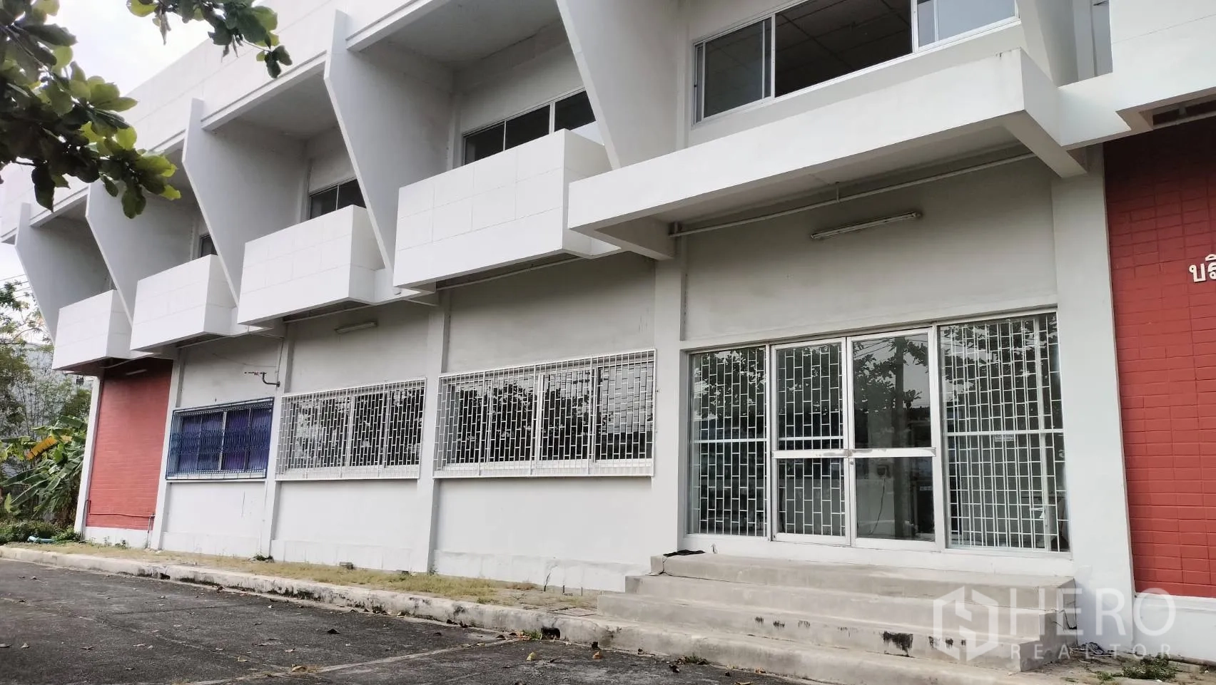 Factory for rent in Lat Krabang, Bangkok - Front facade with metal security grilles and a stepped entrance to glass doors.
