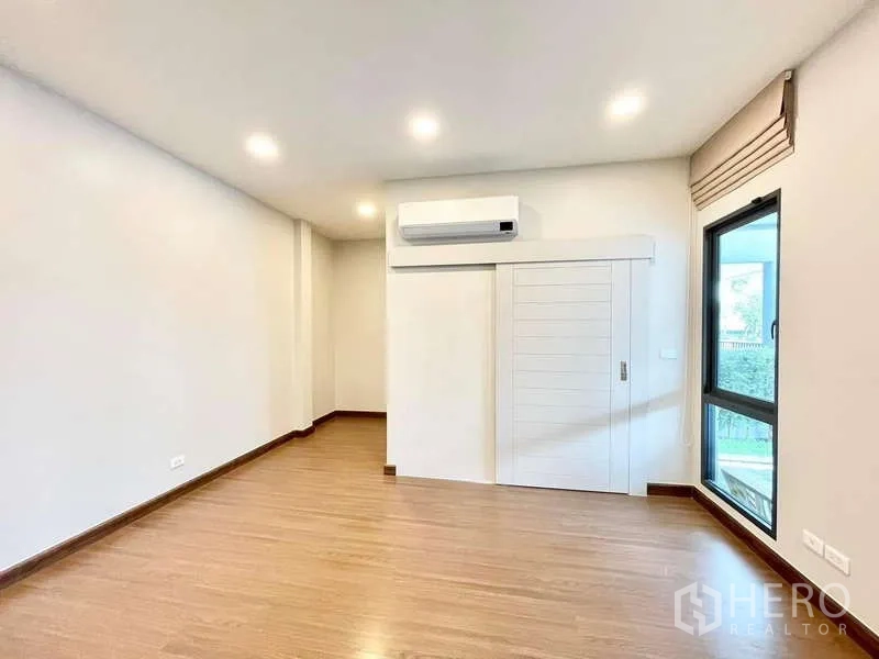 Detached House for rent in Bang Phli, Samut Prakan - Empty multipurpose room with wood flooring, AC unit and tall window.