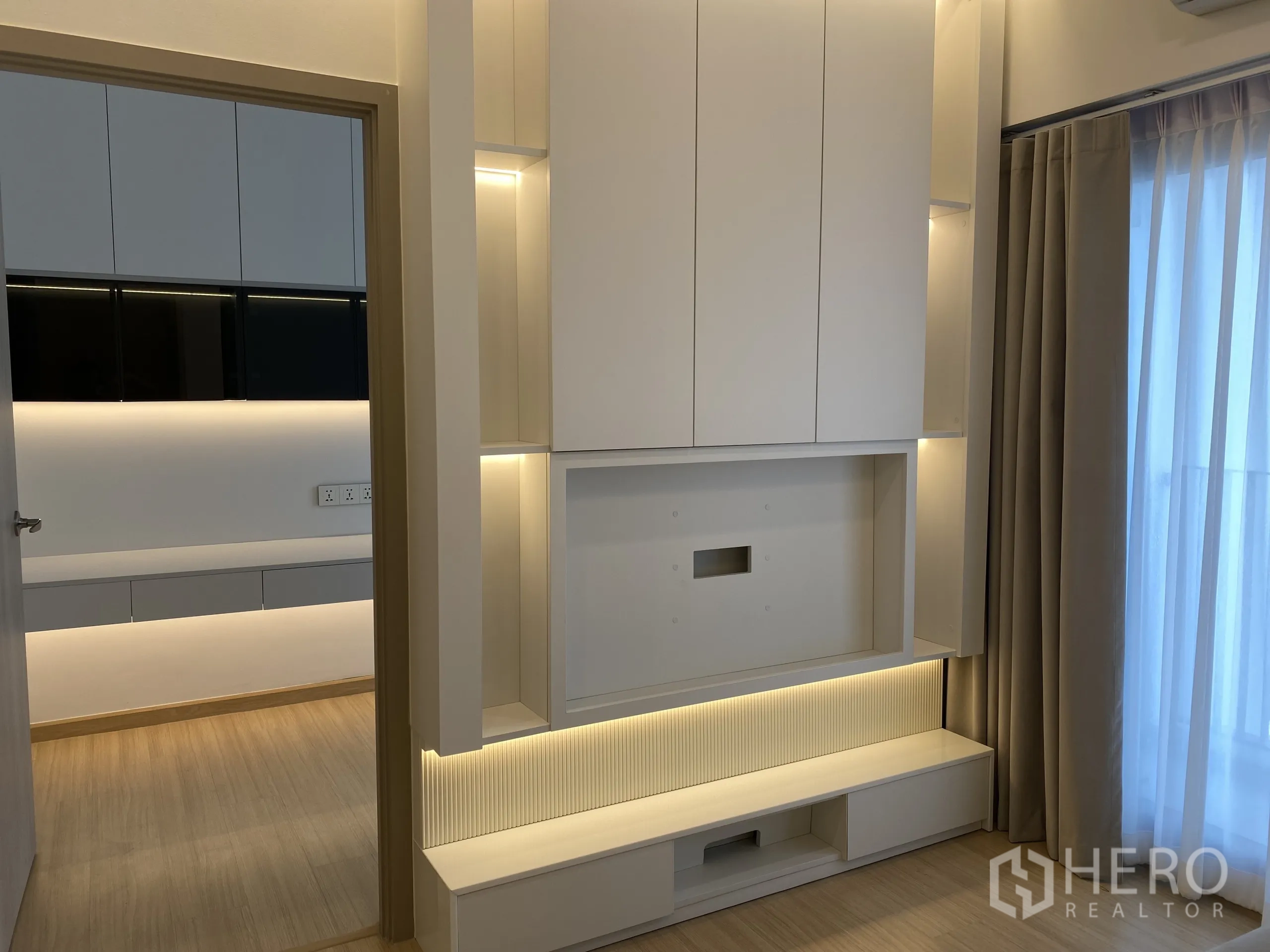 คอนโด ให้เช่าในPhra Khanong, Bangkok - ผนังทีวีบิวท์อินพร้อมตู้เก็บของและไฟซ่อน ข้างผ้าม่านโปร่งริมระเบียง