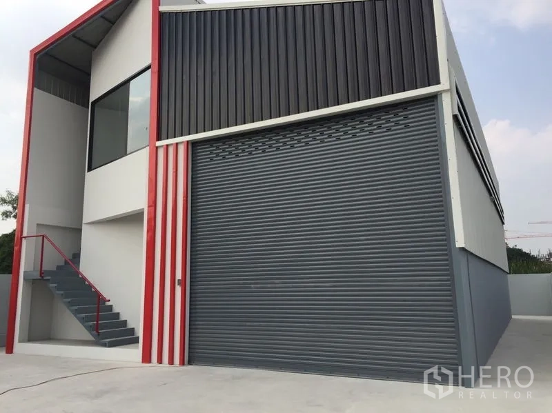 货栈 出售在Khlong Luang, Pathum Thani - 现代仓库立面，宽卷帘门与红色框架。