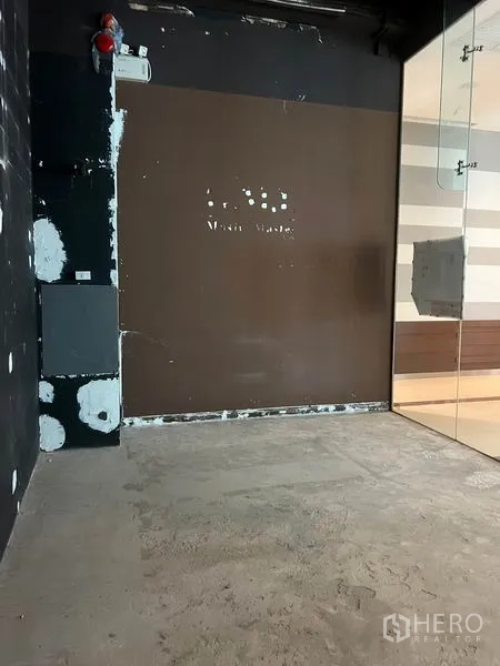 零售空间 出租在Watthana, Bangkok - 空置商铺后墙，棕色护墙板与安全设备，玻璃隔断入口一览无遗。