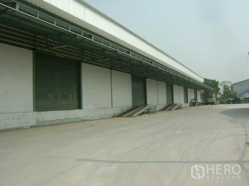 货栈 出租在Mueang Samut Sakhon, Samut Sakhon - 仓库长立面，多个装卸平台，前方宽阔车道可容拖车。
