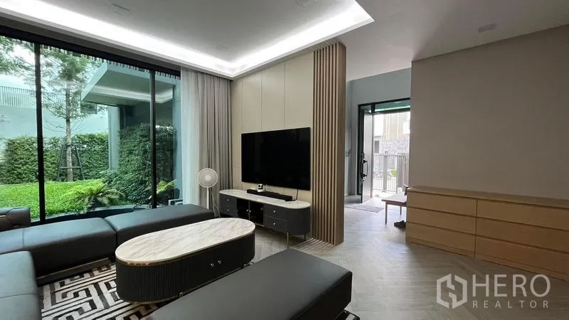 Detached House for sale in Saphan Sung, Bangkok - Living area view showing TV feature wall, sheer curtains and garden through wide sliding doors.