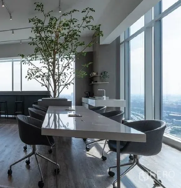 Office Space for rent - Modern office lounge with long table, indoor tree, pantry and floor-to-ceiling windows overlooking Bangkok.