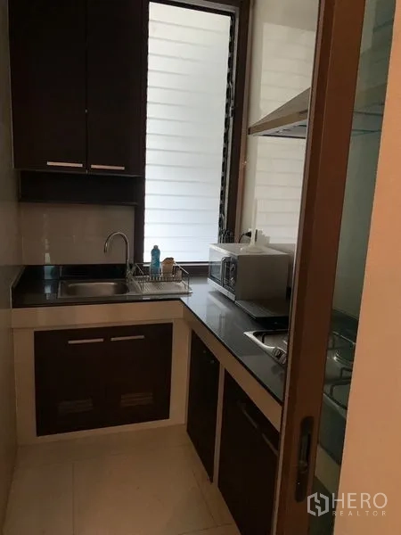 Townhouse for sale in Watthana, Bangkok - Second view of the galley kitchen with dark cabinetry, sink and cooktop by the window.