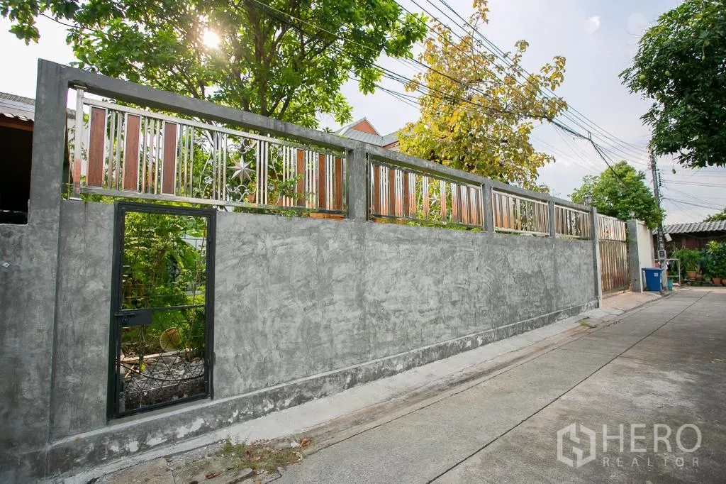 Detached House for rent or sale in Huai Khwang, Bangkok - Solid concrete perimeter wall with decorative metal panels and a pedestrian door.