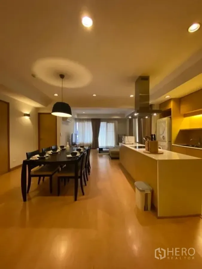 公寓 出租在Watthana, Bangkok - 开放式餐厅配六人餐桌，旁为带岛台的现代厨房与暖色灯光。