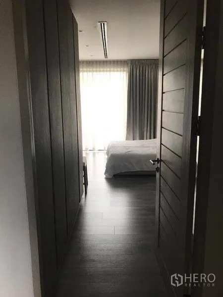 Townhouse for rent in Khlong Toei, Bangkok - View through doorway to a bedroom with floor-to-ceiling curtains and wood flooring.