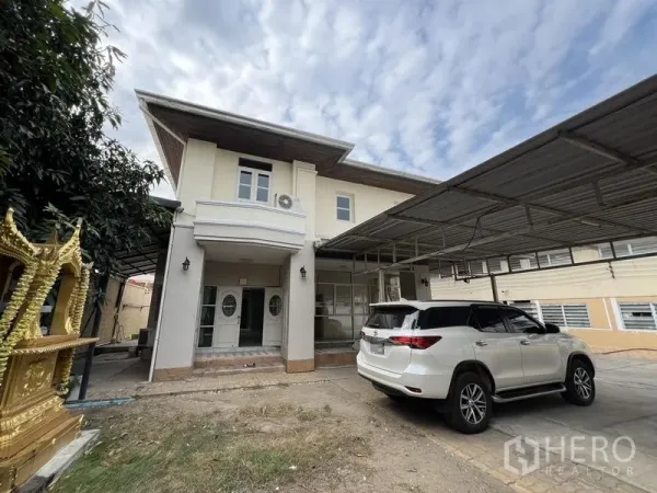 บ้าน ให้เช่าหรือขายในLak Si, Bangkok - ด้านหน้าบ้านสองชั้นมีชานเสาโค้ง ประตูกระจก และพื้นที่จอดรถมีหลังคาขนาดใหญ่