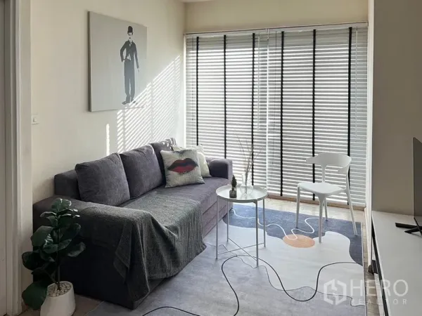 公寓 出租在Khlong Toei, Bangkok - 采光充足的客厅，灰色沙发、挂画、整面落地窗百叶与小圆几。