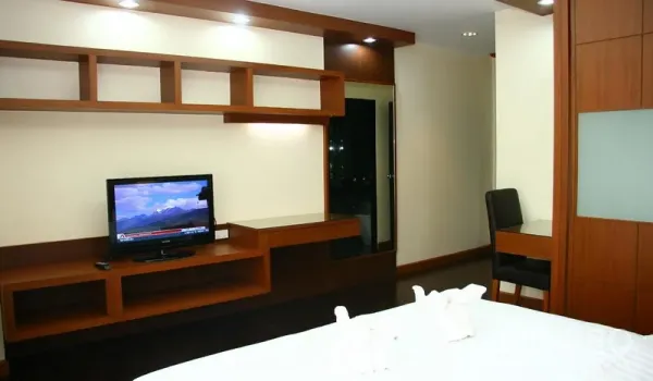 Apartment for rent in Khlong Toei, Bangkok - Ekkamai apartment bedroom with built-in wooden TV wall and desk under recessed lighting