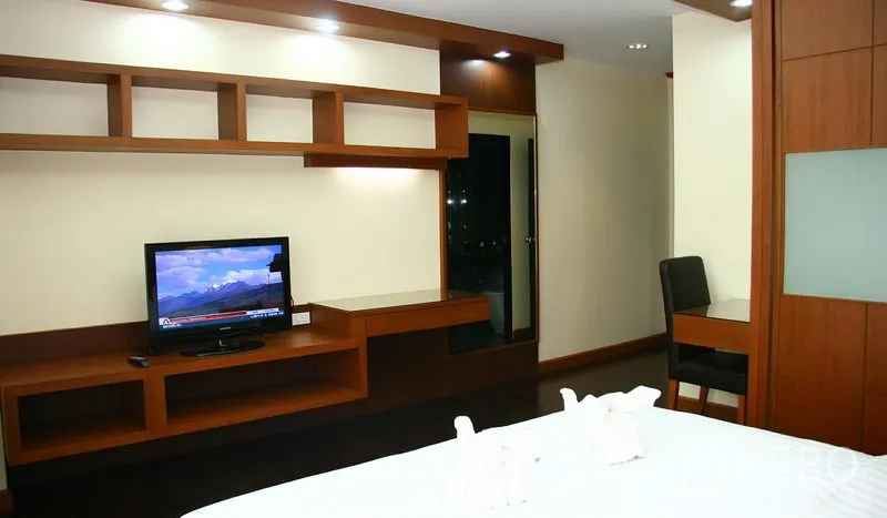 Apartment for rent in Khlong Toei, Bangkok - Ekkamai apartment bedroom with built-in wooden TV wall and desk under recessed lighting