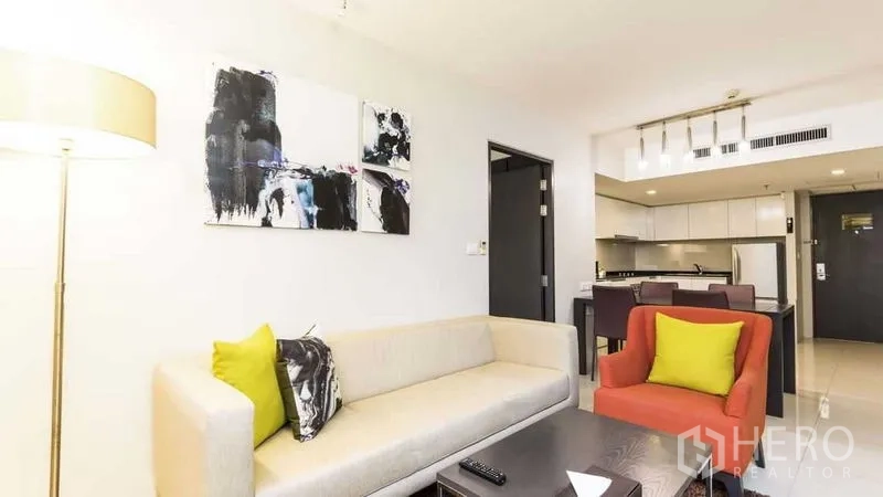 Apartment for rent in Watthana, Bangkok - Living area with sofa, artwork and floor lamp facing the dining and kitchen.