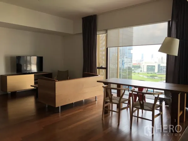 公寓 出租在Pathum Wan, Bangkok - 开放式客餐厅，实木地板、电视柜，落地窗俯瞰城市与绿地景观