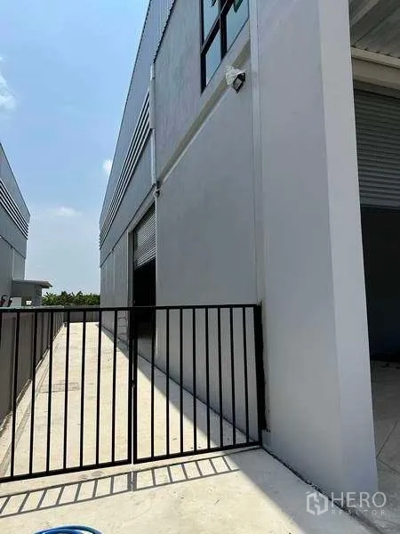 Factory for rent or sale in Bang Bo, Samut Prakan - Gated side access with roller shutter door along the factory wall.