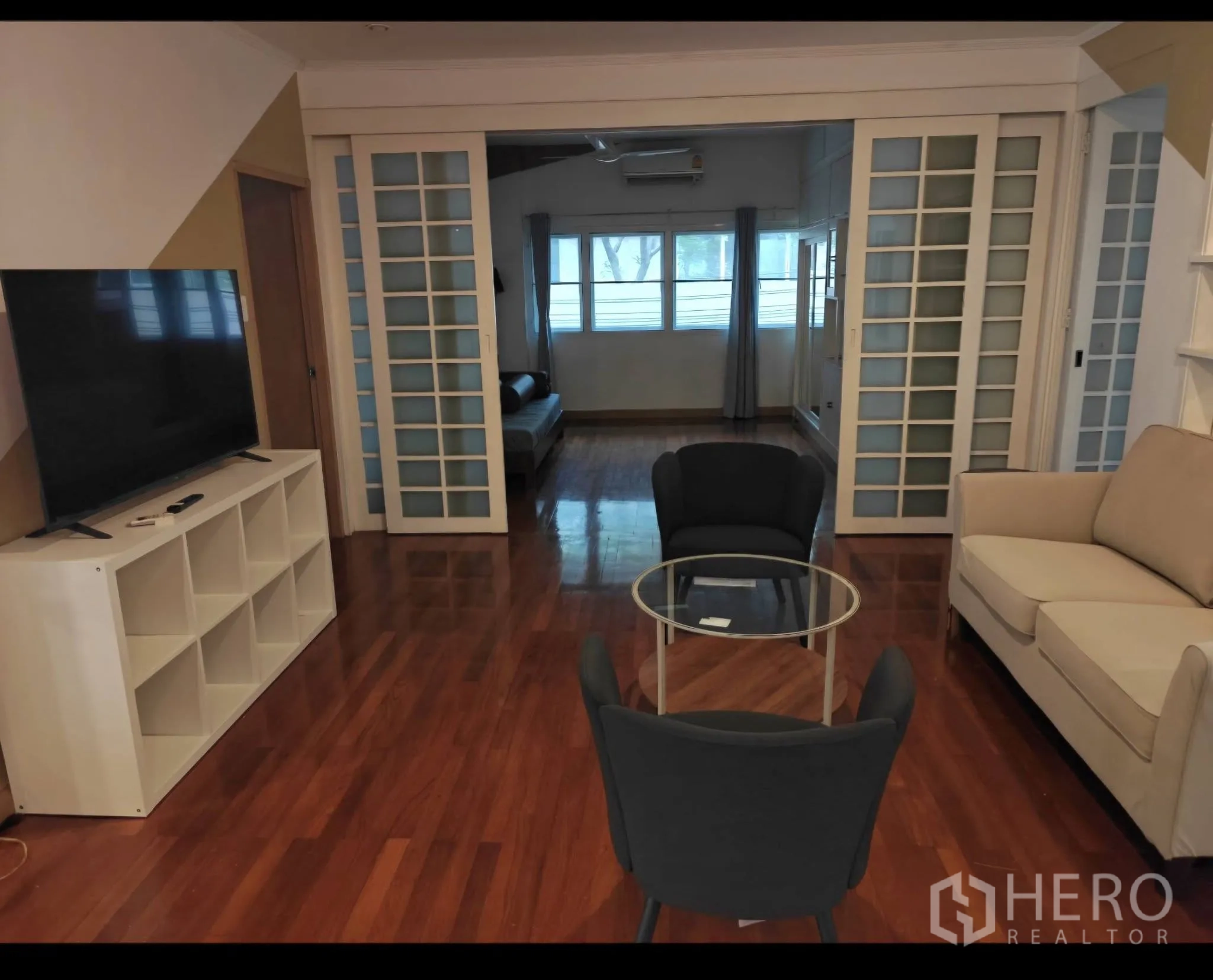 Condominium for rent in Sathon, Bangkok - TV lounge with sofa, glass coffee table, and sliding partitions to a multipurpose room.