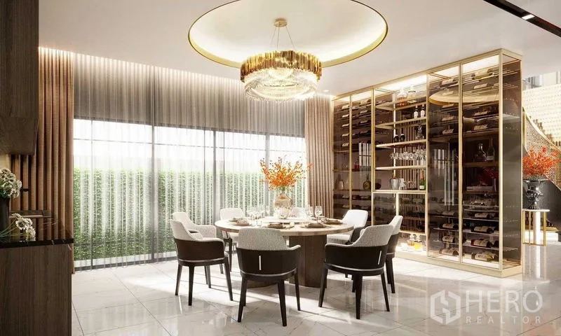 Detached House for sale in Prawet, Bangkok - Sunlit dining room with round table, gold chandelier and glass wine display wall.