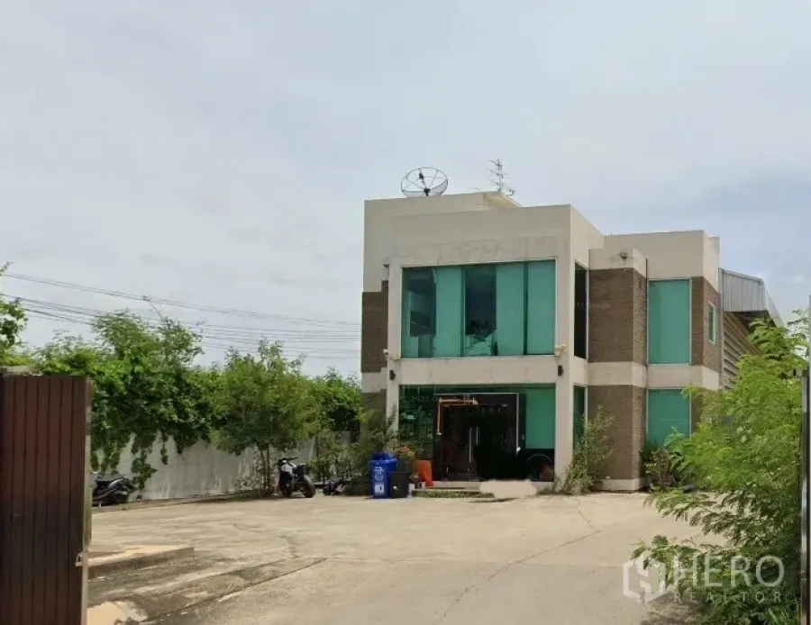 工厂 出租在Bang Bua Thong, Nonthaburi - 暖武里邦武通两层厂房办公楼，绿色玻璃立面，宽阔混凝土院场与大门入口。