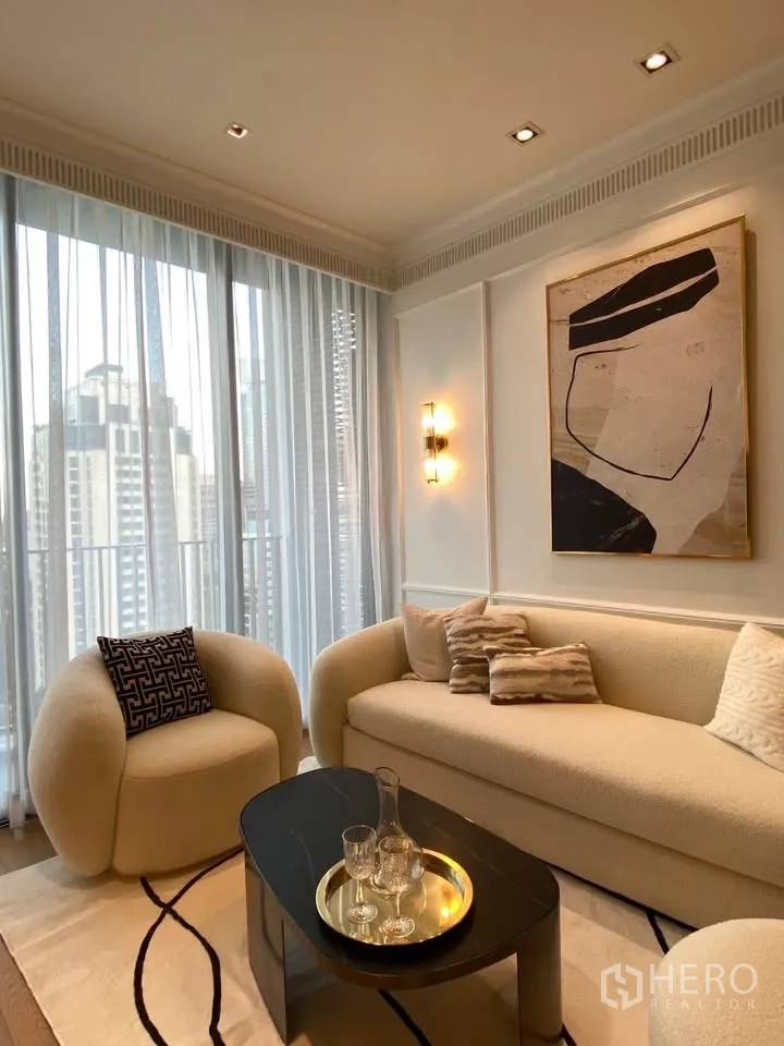Condominium for rent in Pathum Wan, Bangkok - Cozy living area with curved armchair and sofa, coffee table, sheer curtains, and city backdrop.
