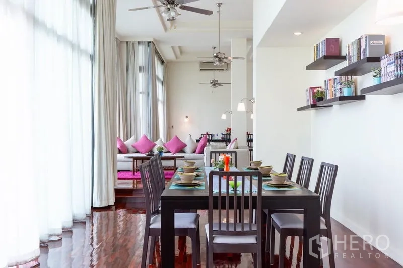 Condominium for rent in Bang Rak, Bangkok - Dining room leading to the living area with tall curtains, ceiling fans and glossy timber flooring.