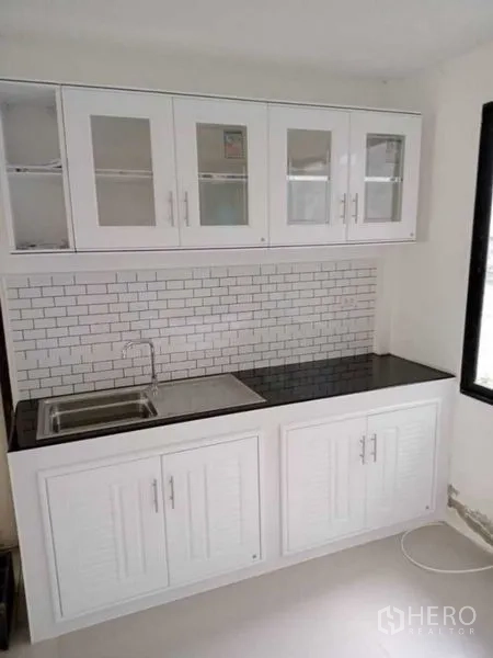 Detached House for rent in Prawet, Bangkok - Kitchen sink with upper glass cabinets, black countertop and white subway tile wall.