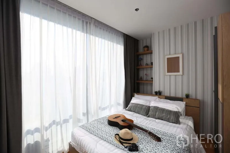 Condominium for sale in Bang Rak, Bangkok - Bedroom with full-height sheer curtains and natural light over a double bed.
