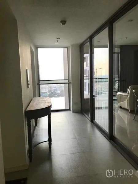 คอนโด ให้เช่าในBang Kho Laem, Bangkok - โถงทางเดินมีหน้าต่างสูงจรดเพดานและฉากกั้นกระจกไปยังส่วนรับแขก พร้อมโต๊ะคอนโซล.