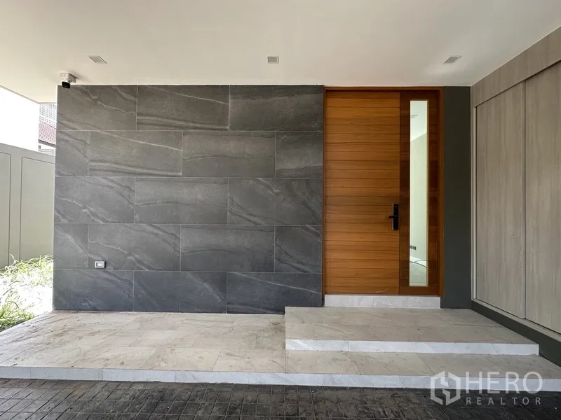 โฮมออฟฟิศ for rent or sale in Suan Luang, Bangkok - ทางเข้ามีผนังหินสีเข้มและประตูไม้ใต้ชายคา